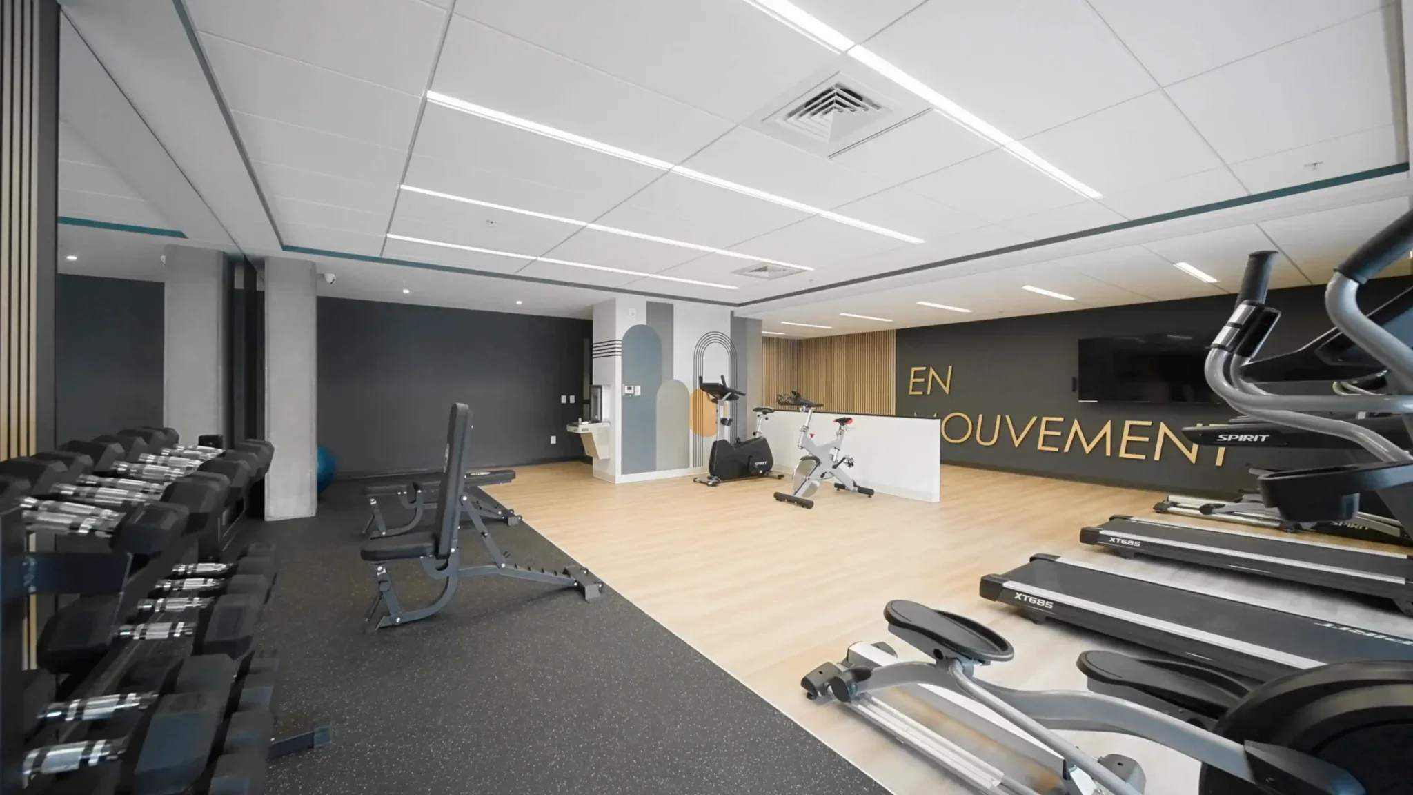 Salle de sport équipée de machines cardio et musculaires avec mur décoratif "En Mouvement"